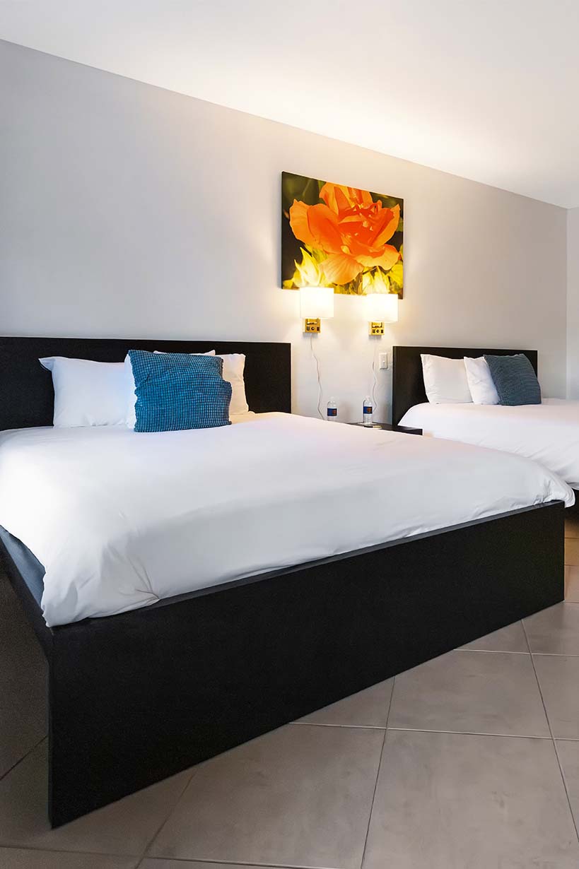 A clean and modern hotel room with two beds, two headboards, and a piece of artwork on the wall.